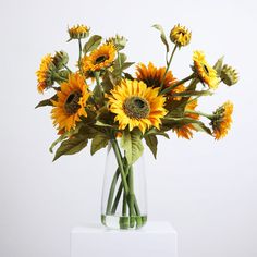 a vase filled with yellow sunflowers on top of a white countertop next to a wall