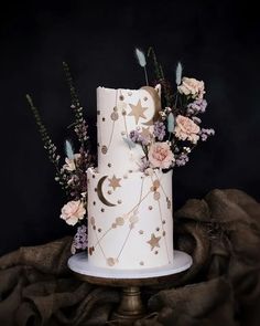 a white and gold decorated cake with flowers on the top is sitting on a table