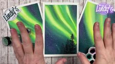 someone holding up two cards with green and purple aurora bores in the night sky