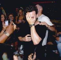 a man covering his face while standing in front of a group of people holding cell phones