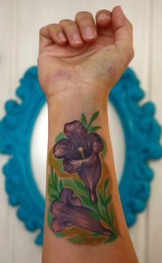 a woman's arm with purple flowers on it and green leaves around the wrist