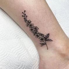 a black and white flower tattoo on the ankle, with small flowers growing out of it