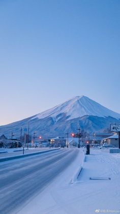 a snow covered road with a mountain in the background at dusk, and street lights on either side