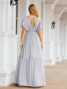 a woman in a gray dress standing on the porch with her back to the camera