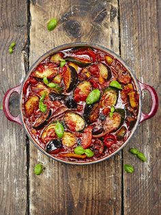 a red pot filled with cooked vegetables on top of a wooden table next to green peppers