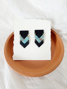 a pair of black and blue earrings sitting on top of a brown plate next to a white sheet