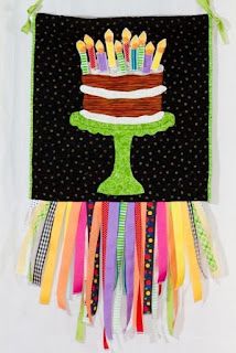 a birthday cake with candles on it hanging from a green ribboned wall hanger