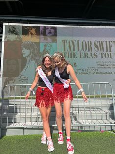 two women in red fringe skirts standing next to each other on a stage with a banner behind them