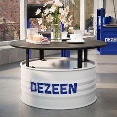 there is a table with flowers and cups on it in front of a window that says dezeen