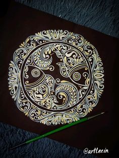 an intricately designed piece of art on a black surface with a green pencil next to it