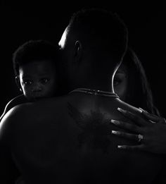 a black and white photo of a woman holding a baby in her arms with the man's arm wrapped around him