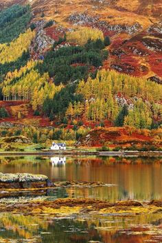 a small house sitting in the middle of a lake surrounded by mountains and trees with autumn colors