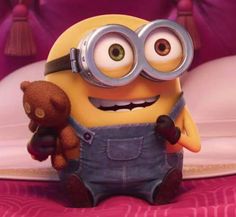 a minion holding a teddy bear on top of a bed