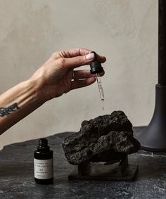 a person is holding a small bottle with some liquid in it next to a rock