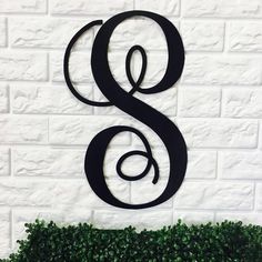 the letter s is made out of metal and sits in front of a white brick wall