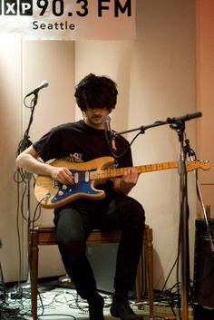 a man sitting in front of a microphone while playing an electric guitar with headphones on