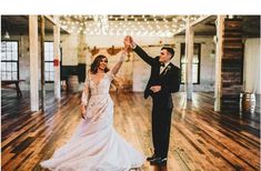 a bride and groom are dancing together in an old building with string lights hanging from the ceiling