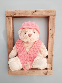 a teddy bear wearing a pink hat and scarf in a wooden frame on the wall