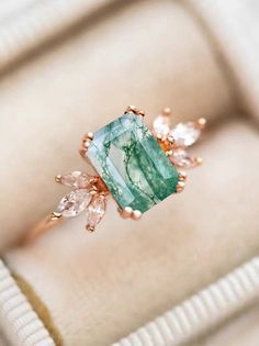 a ring with an emerald stone surrounded by white and pink stones on top of it