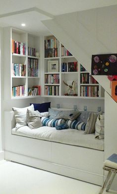 a room with bookshelves and a bed in the corner, under some stairs