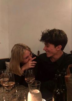 a man and woman sitting at a table with wine glasses in front of their faces