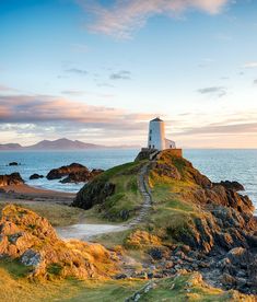 a lighthouse on top of a rocky outcropping by the ocean at sunset