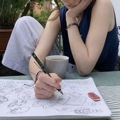 a woman sitting at a table writing on a piece of paper with a cup of coffee in front of her