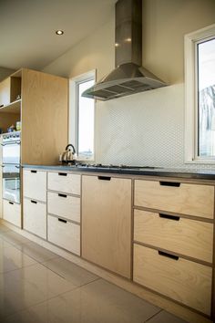 a kitchen with wooden cabinets and stainless steel range hood over the stove top, in front of a large window