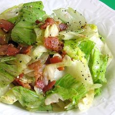 a white bowl filled with lettuce and bacon on top of a green table