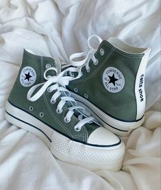 a pair of green converse sneakers sitting on top of a bed