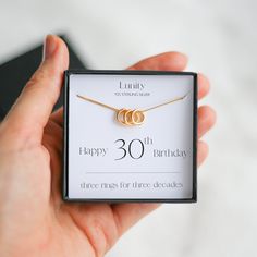 a person holding a box with a necklace on it that says 30 th birthday and two rings for three decades