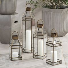 three metal lanterns with candles in them sitting on the ground next to a potted plant