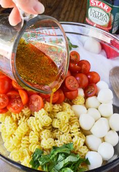 someone pouring dressing into a bowl filled with pasta and tomatoes, mozzarella shells, spinach sprinkled with parsley