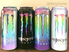 four cans of monster energy drink are lined up on a wooden table in front of a wall