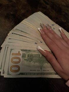 a woman's hand with white nails holding money