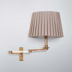 a wall lamp with a beige shade on it and a gold cross hanging from the side