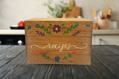 a wooden box sitting on top of a table with flowers painted on the lid and writing