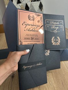 a person holding up some black and gold wedding cards