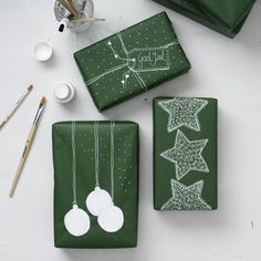 green wrapping paper with white stars and ornaments on it, next to paintbrushes