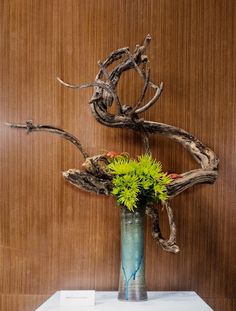 a vase filled with flowers sitting on top of a white table next to a wooden wall