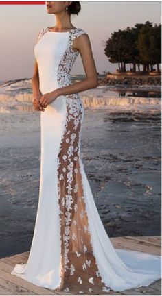 a woman in a white and brown dress standing on the beach with her back to the camera