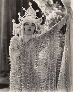 an old photo of a woman wearing a tiara and holding her hands up in the air