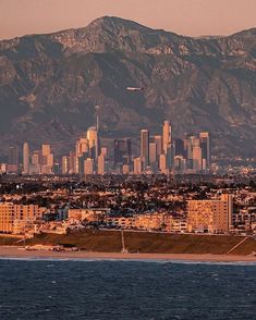 an airplane flying over a city with mountains in the back ground and water below it