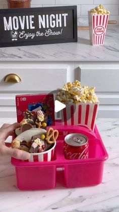 a pink tray with popcorn, pretzels and movie tickets in it on a white countertop