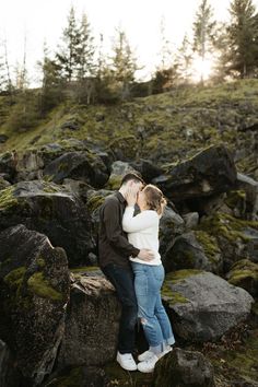 an engaged couple kissing on rocks in the woods