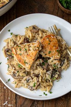 a white plate topped with pasta and meat covered in mushroom sauce next to a fork