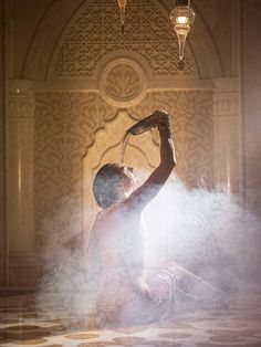 a man sitting on the ground with his arms in the air while spraying water onto his face