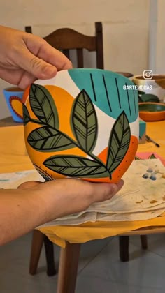 a person holding a bowl with leaves painted on it and another hand reaching out to the bowl