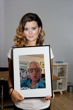 a woman holding up a framed photo of an older man