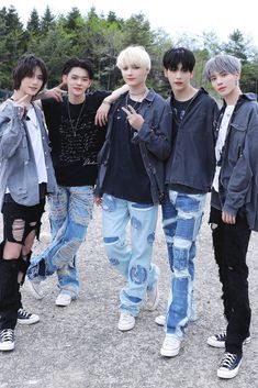 four young men standing next to each other in front of trees and dirt ground with one man wearing ripped jeans